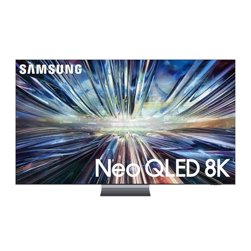 Una TV Samsung QLED da 85 pollici è montata su una parete bianca in un soggiorno elegante, con un divano grigio e un tavolino in legno chiaro. La stanza è ben illuminata da una finestra.