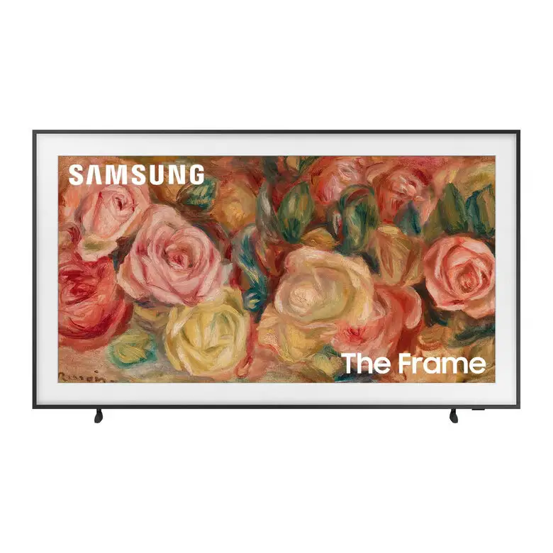 Una TV Samsung QLED 4K è appesa a una parete bianca in un salotto elegante. Il divano grigio è posizionato di fronte alla TV, con un tappeto chiaro e decorazioni minimaliste intorno.