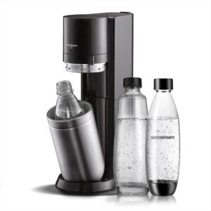 Un dispositivo SodaStream Duo di colore nero e acciaio è posizionato su un piano di lavoro in cucina, circondato da bottiglie di acqua e ingredienti per la preparazione di bevande frizzanti.