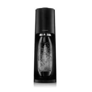 Un gasatore di acqua Sodastream di colore nero è posizionato su un piano di lavoro in cucina, circondato da bottiglie di vetro e un bicchiere. L'ambiente è luminoso e moderno.