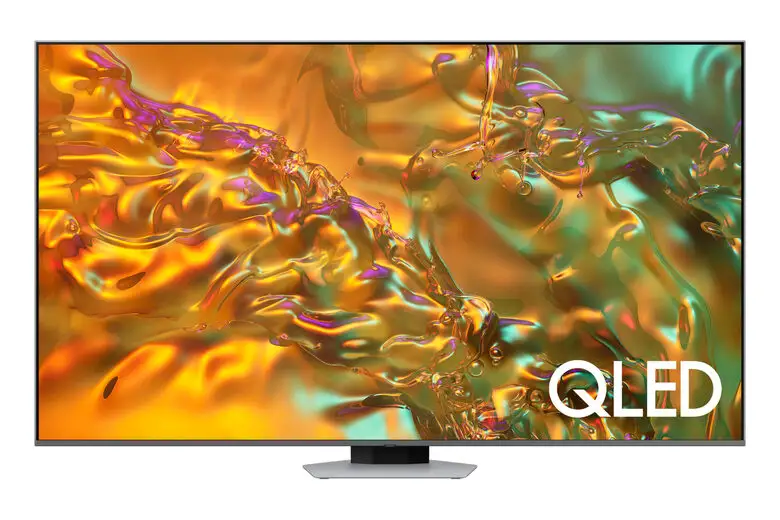 Una TV Samsung Q80D QLED 4K è appesa a una parete in un soggiorno elegante, con un divano grigio e decorazioni minimaliste. La luce naturale entra dalle finestre, creando un'atmosfera accogliente.