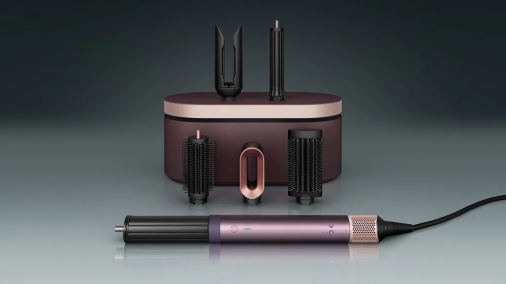 Una giovane donna con capelli mossi utilizza un dispositivo per acconciature, circondata da un ambiente luminoso e ordinato, con un grande specchio e prodotti per capelli visibili.